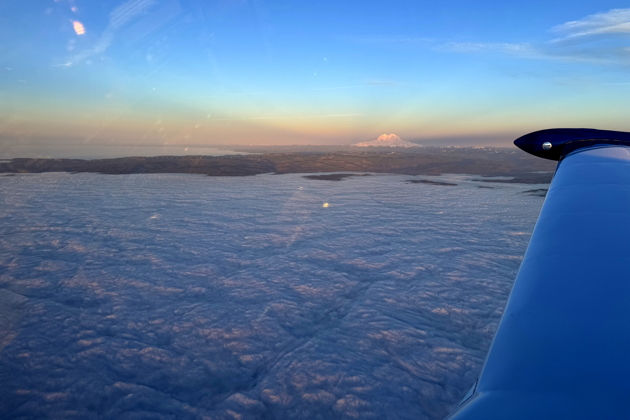 Our view from the Comanche over Toledo, WA, looking northeast over a sea of white and Mt. Rainier, with only the ridge and wind turbines east of Tenino sticking out above the clouds. My photo.